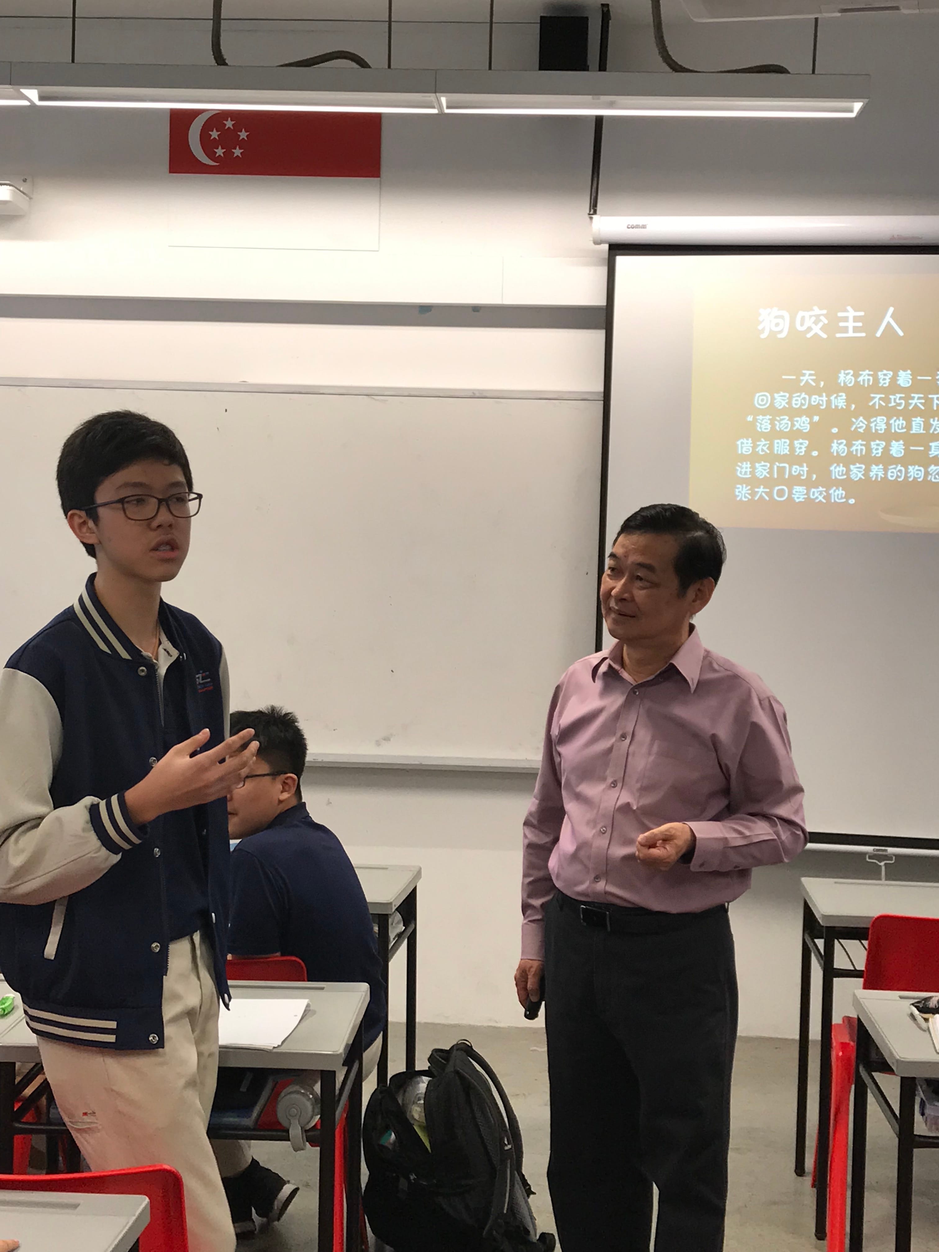 A teenage boy and an older man stand in a classroom with a whiteboard and Chinese text on a projected screen.